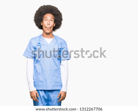 Young african american doctor man with afro hair making fish face with lips, crazy and comical gesture. Funny expression.