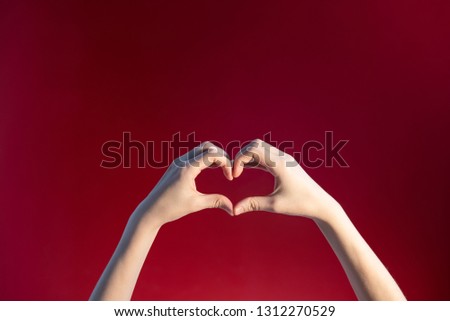 Heart made up of female hands on a red background. Conceptual minimalistic photo with a empty space for placing objects.