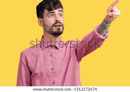Young handsome man wearing pink shirt over isolated background Pointing with finger surprised ahead, open mouth amazed expression, something in front