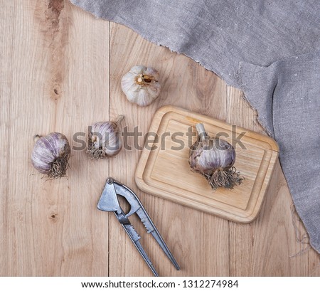 unpeeled fresh garlic fruits and iron hand press,  wooden background 