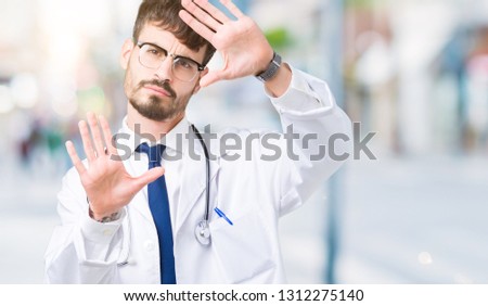 Young doctor man wearing hospital coat over isolated background Smiling doing frame using hands palms and fingers, camera perspective