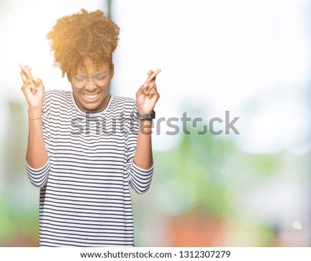Beautiful young african american woman wearing glasses over isolated background smiling crossing fingers with hope and eyes closed. Luck and superstitious concept.