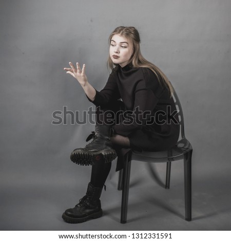 girl in a black dress on a gray background sitting on a chair