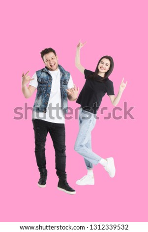 young couple crazy  in jeans and 
t-shirts casual clothes  standing and smiling together on pink background gesturing with hands