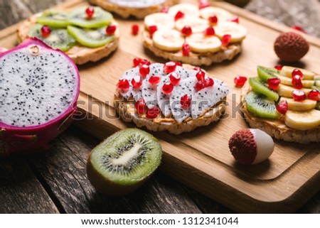 Healthy organic and vegan breakfast. Mini sandwiches with peanut butter and fruits. Fruit summer snack. Sandwiches with dragon fruit, banana, kiwi and pomegranate on wooden table. Fruits diet
