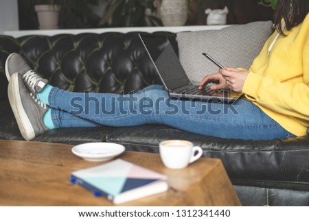 Profile side view cropped photo of unrecognizable lady person in stylish trendy denim jeans wear. She sitting couch inside loft interior restaurant and using laptop with portable telephone equipment