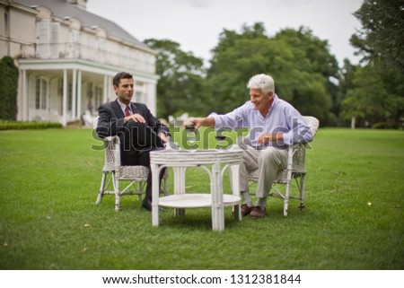 Smiling senior man pouring a glass of wine while he sits with his mid-adult son outside in the garden.