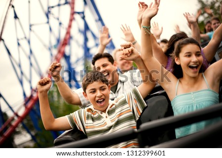 Smiling family riding on a rollercoaster at an amusement park. Royalty-Free Stock Photo #1312399601