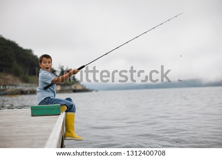 Portrait of a surprised boy fishing off the side of a jetty with a fishing rod.