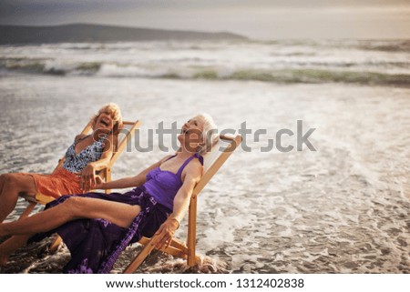 Two happy mature women relaxing in deck chairs on the beach.