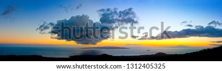 Scenic view of coastline under dramatic clouds at sunset.