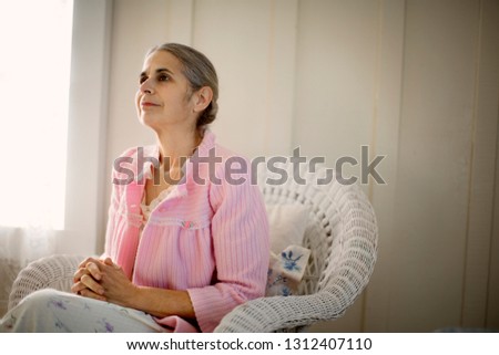 Contemplative senior woman sitting in an armchair with her hands clasped.