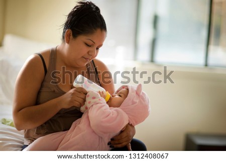 Young mother sitting on the bed giving her baby daughter a bottle.