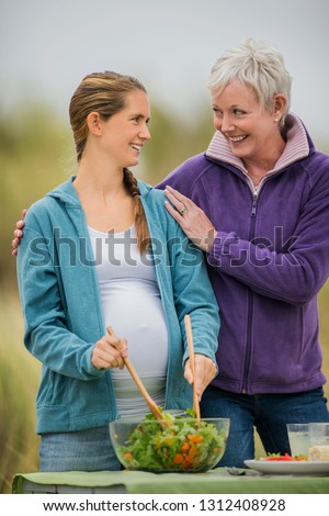 Cheerful mature woman chats with her pregnant daughter as they prepare an outdoor lunch.