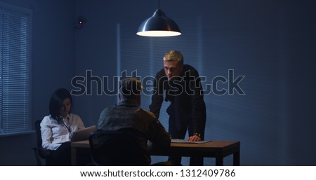 Medium shot of a male and a female investigator interrogating a soldier Royalty-Free Stock Photo #1312409786