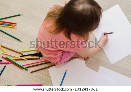 little girl draws with colored pencils on the floor
