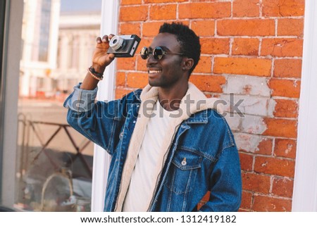 Portrait happy smiling african man photographer with vintage film camera taking picture walking on city street over brick wall background