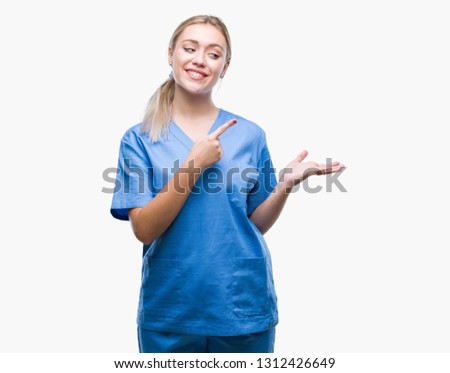 Young blonde surgeon doctor woman wearing medical uniform over isolated background amazed and smiling to the camera while presenting with hand and pointing with finger.