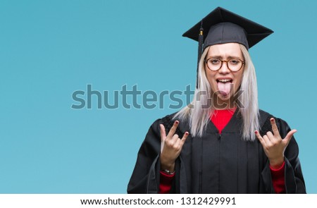 Young blonde woman wearing graduate uniform over isolated background shouting with crazy expression doing rock symbol with hands up. Music star. Heavy concept.