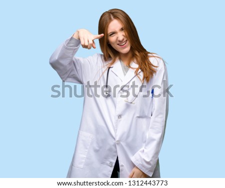 Redhead doctor woman frustrated by a bad situation and pointing to the front on isolated blue background