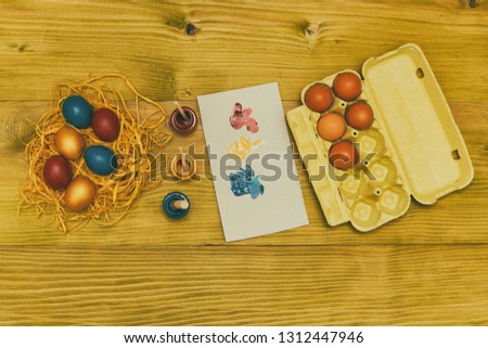 Painted Easter eggs in straw,eggs and colors for painting on wooden table.Toned photo.