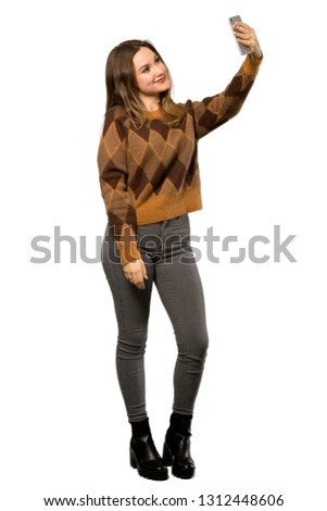 A full-length shot of a Teenager girl with brown sweater making a selfie over isolated white background
