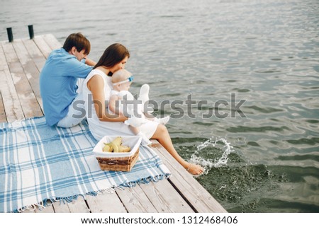 Cute family near water. Beautyful mother with her little daughter. Hundsome man in a blue shirt. Picnic near lake