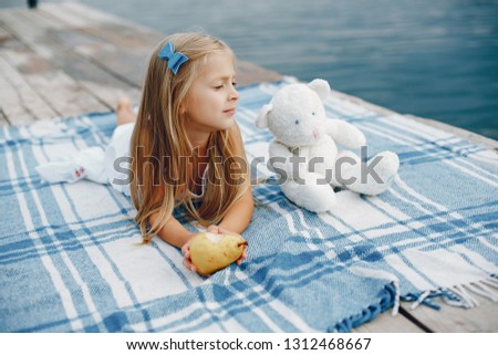 Cute little girl in a white dress. Child sitting near water. 