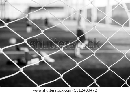 black and white picture of mesh of goal with blurry of soccer goalkeeper and soccer players. Soccer ball training in academy.