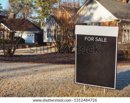 Close up shot of black color blank For Sale sign on the yellow color yard in winter season with nice house and neighbor in the background