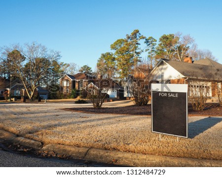 Wide shot of black color blank For Sale sign on the yellow color yard in winter season with nice house and neighbor in the background