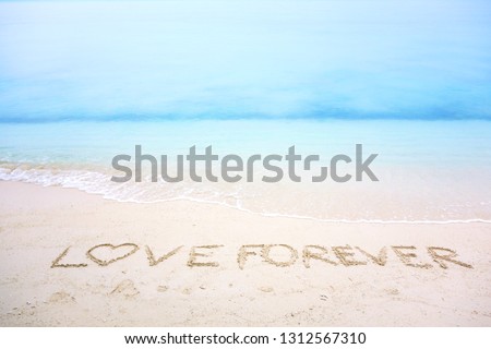 Happy Valentines day, LOVE lettering on the beach with wave and clear blue sea. Heart shape message written in white sand on romantic beach background. Concept for love and Valentines day. Copy space.