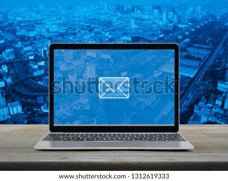 email flat icon with modern laptop computer on wooden table over city tower, street, expressway and skyscraper, Business contact us online concept
