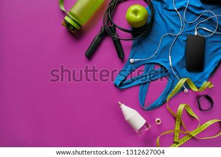 Health fitness background. Sneakers, dumbbell, power grip, green apple, water bottle, blue shirt, phone and earphone on dark background.