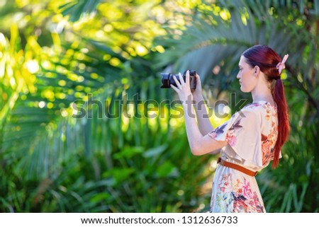 Pretty young girl in a floral summer dress out in the garden taking photos with her camera