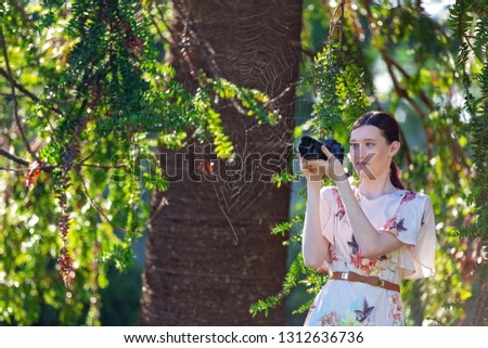 Beautiful young girl taking photo of a cobweb amongst the trees in the garden