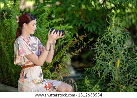 Pretty girl taking photos in a sunlit garden with her digital camera