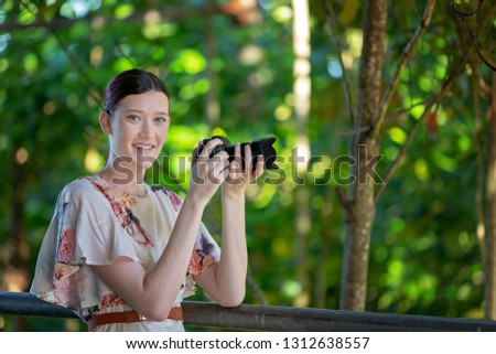 Pretty smiling girl taking photos in a sunlit garden with her digital camera