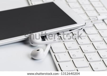 white earphones on white keyboard with phone