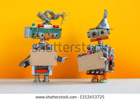 Comical robots with a cardboards mockup. Creative design robotic toys holding a blank empty paper posters, yellow wall background. copy space for text and design elements.