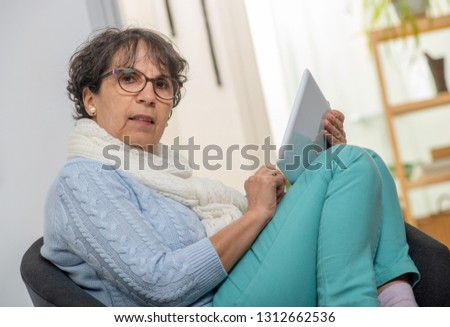 charming senior brunette woman with glasses using a digital tablet at home