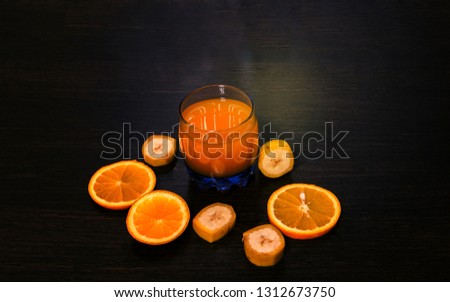 A glass of fruit juice and sliced orange and banana on a dark wooden surface.