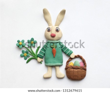 A cute hare in a blue dress with a basket of Easter eggs and flowers. Plasticine character on a white background Royalty-Free Stock Photo #1312679615