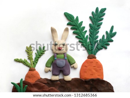 Bunny in overalls in the garden with carrots. Plasticine illustration Royalty-Free Stock Photo #1312685366