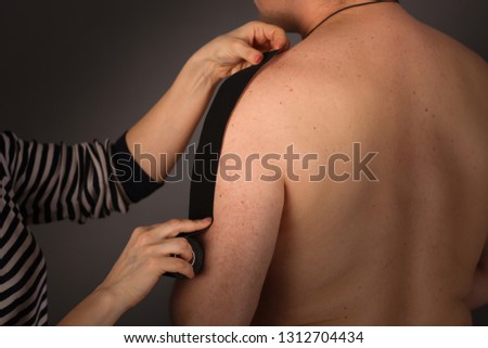 Shoulder Taping Beautiful slender woman puts tapes on the arm of an ordinary man, concept alternative medicine