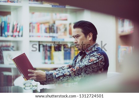 Senior asian man reading with presbyopia in library, process color.