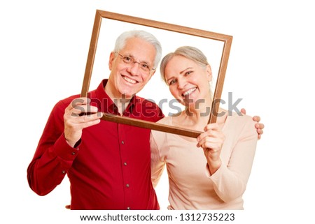 Happy seniors couple is looking through a blank picture frame