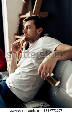man eating tasty pizza and holding bottle in living room
