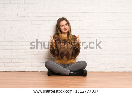 Teenager girl sitting on the floor with thumbs up because something good has happened