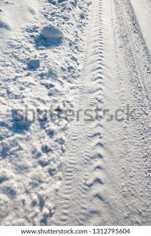 the trace on snow from a tread of the car on the winter road slightly powdered with snow. visible to the side of the road.